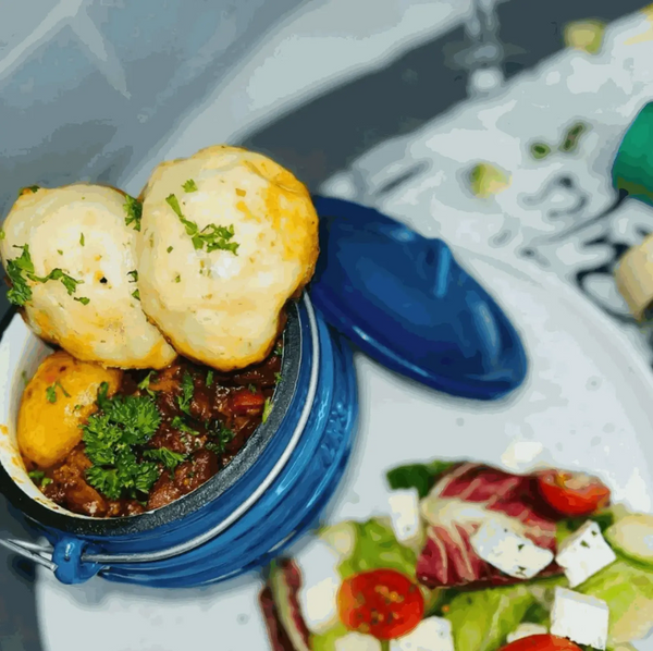 Blue 3-legged cast iron pot with stew and dumplings, featuring a handle and lid, perfect for outdoor cooking.