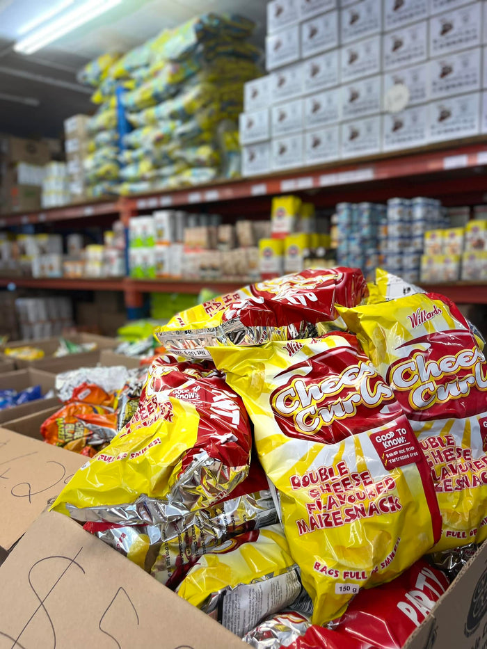 Fully stocked shelves of South African snacks and groceries at Something From Home warehouse with Cheese Curls in the foreground