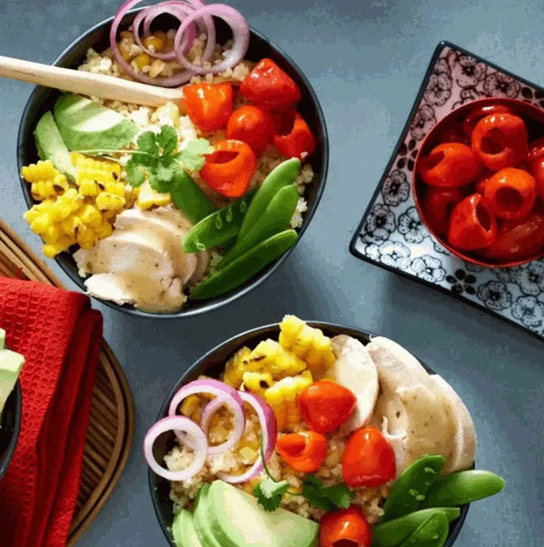 Bowl of salad with PEPPADEWS mild whole peppers, grilled corn, avocado, chicken, onions, and snap peas with extra PEPPADEWS on the side